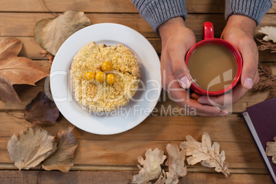 Hand of man holding cup of coffee with breakfast and autumn leaves on table