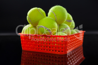 Close up of fluorescent yellow tennis balls in red plastic basket with reflection