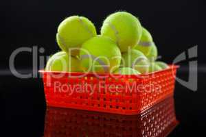 Close up of fluorescent yellow tennis balls in red plastic basket with reflection