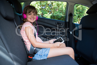 Teenage girl in headphones using digital tablet in the back seat of car