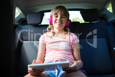 Teenage girl in headphones using digital tablet in the back seat of car