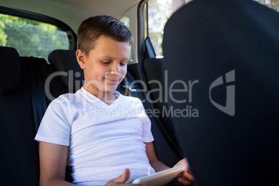 Teenage boy using digital tablet in the back seat of car