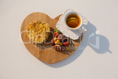 Various fruits, sweet food and cup of green tea on chopping board