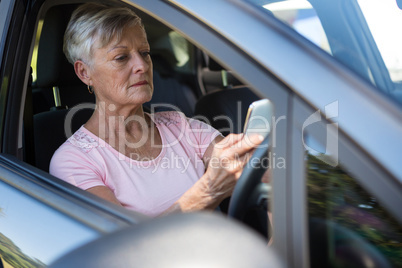 Senior woman using mobile phone while driving car