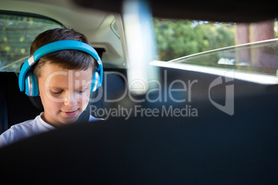 Teenage boy with headphones sitting in the back seat of car