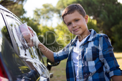 Teenage boy washing a car on a sunny day