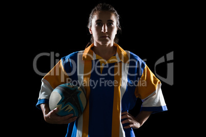 Portrait of female rugby player holding ball while standing with hand on hip