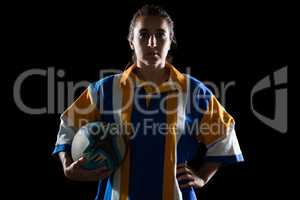 Portrait of female rugby player holding ball while standing with hand on hip