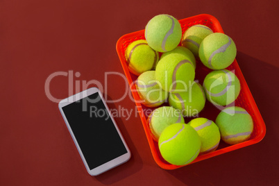 High angle view of tennis balls in red basket by mobile phone