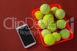 High angle view of tennis balls in red basket by mobile phone