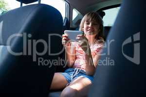 Teenage girl in headphones using mobile phone in the back seat of car