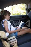 Teenage girl reading book in the back seat of car