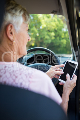 Senior woman using mobile phone while driving a car