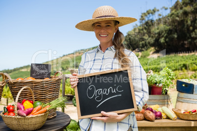 Portrait of happy woman holding slate with text in vineyard