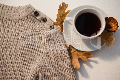 Cup of black tea with autumn leaves and woolen cloth on white background