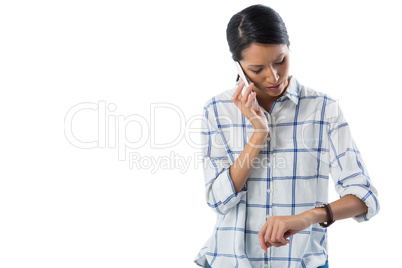 Female executive looking at her wristwatch while talking on the phone