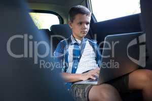 Teenage boy using laptop in the back seat of car