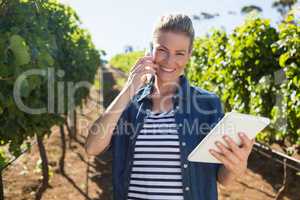 Female vintner using digital tablet while talking on mobile phone