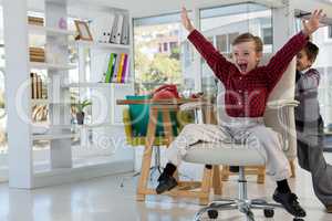 Boy as business executives pushing his colleague on chair