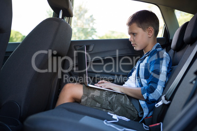 Teenage boy using laptop in the back seat of car