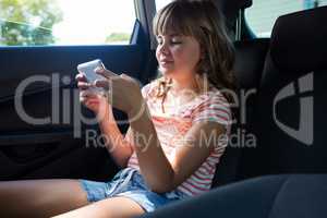 Teenage girl using mobile phone in the back seat of car