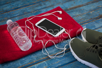 High angle view of water bottle with mobile phone and in-ear headphones on napkin by sports shoes