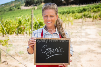 Portrait of happy woman holding slate with text in vineyard