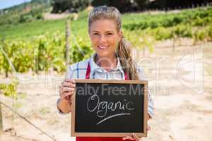Portrait of happy woman holding slate with text in vineyard