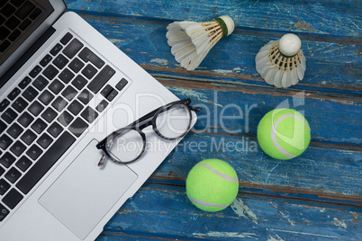High angle view of laptop and eyeglasses with shuttlecocks by tennis balls