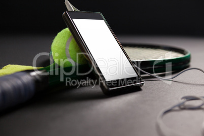 Close up of mobile phone and headphones by tennis ball with racket