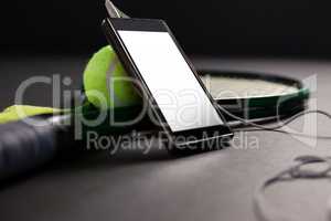 Close up of mobile phone and headphones by tennis ball with racket