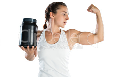 Female athlete flexing muscles while holding supplement jar