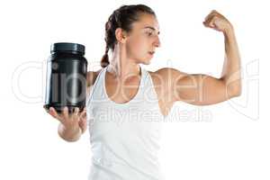 Female athlete flexing muscles while holding supplement jar