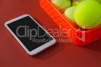 High angle view of tennis balls in red basket by smartphone