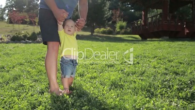 Caring father teaching infant boy to walk on grass