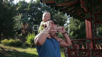 Father carrying cute baby boy on shoulders in park