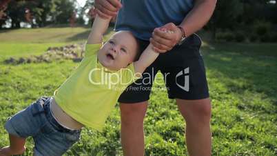 Man swinging his toddler baby boy by hands in park