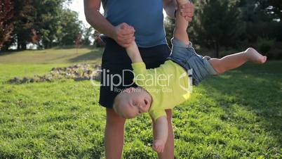 Father swinging toddler son upside down in park