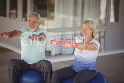 Senior couple sitting on fitness balls with dumbbells