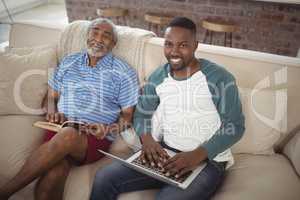 Father and son sitting on sofa with laptop and book in living room