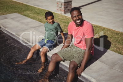 Smiling father and son sitting on edge of swimming pool