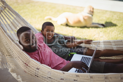 Father and son using laptop while relaxing on hammock