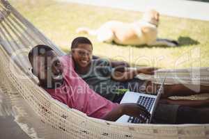 Father and son using laptop while relaxing on hammock
