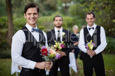 Bridegroom and best man standing with bouquet of flowers in garden