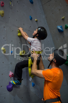 Trainer assisting boy in rock climbing