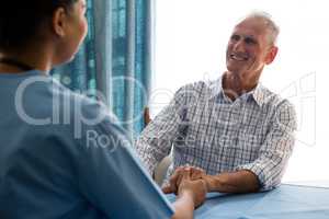 Doctor holding hands of senior man while consoling at table