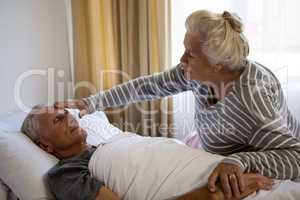 Senior woman sitting by husband sleeping on bed