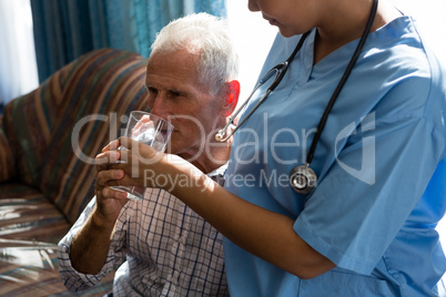 Midsection of female doctor assisting senior man in drinking water