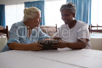 Senior woman showing digital tablet to friend at table