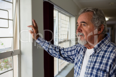 Thoughtful senior man looking through window at nursing home